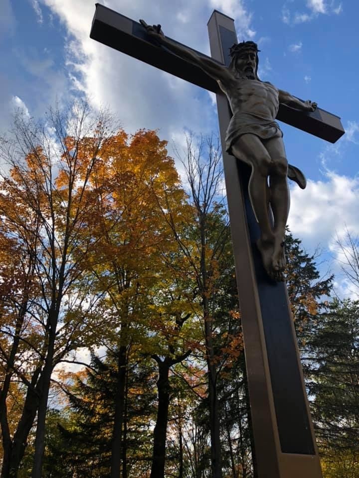A bronze crucifix among autumn trees under a blue sky